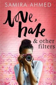 Cover of Love, Hate & other filters by Samira Ahmed. A person with brown skin and dark hair in a bun taking a photo with the camera pointed at the reader. They stand in front of a red wall with colourful tessellating patterns at the bottom. The title and author above.