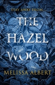 Cover of The Hazel Wood. The title is covered over by silvery-blue leaves. The text reads 'Stay away from... the Hazel Wood.'